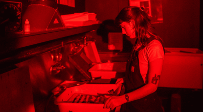 Image of photographer processing images in a darkroom. Red cast on the phhoto/