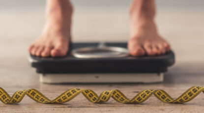 Two feet stand on a scale with a coiled tape measure on the floor