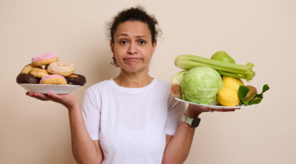 Woman holds two plates: one with donuts, one with vegetables to illustrate "optimism bias."