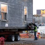 Construction worker winds cable attached to Wallenberg House before the structure is moved from one location in Ann Arbor to another. Michigan Stadium is visible in the background.