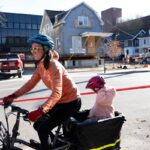 A local Ann Arbor woman rides her bike with baby on board as they pass the Wallenberg House in its new location at Division and Jefferson streets in Ann Arbor.