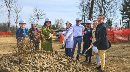 A group of people in hardhats break ground with dirt and shovels.