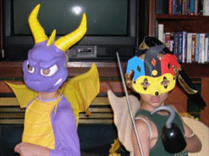 Two kids are dressed up, one likea purple dragon type creature and another like a colorful jester.