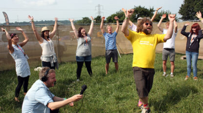 Group of people do laughing yoga in an outdoor venue.