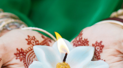 A pair of hands with henna tattoos holds a lotus-shaped candle.