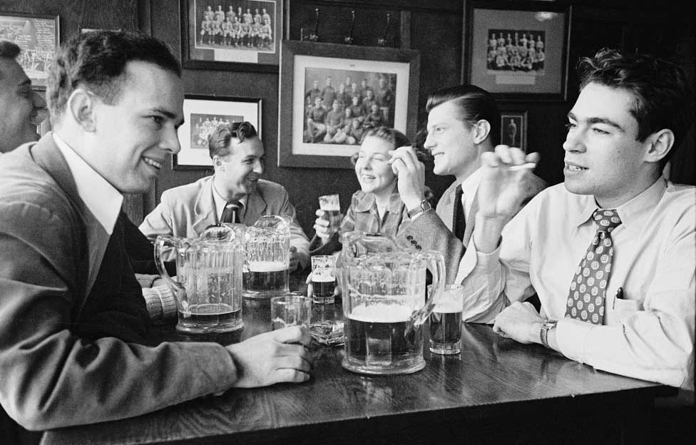 University of Michigan students, circa 1949, in a black and white photo in an Ann Arbor, Michigan, bar. Five caucasian men with pitchers and cigarettes, and one white female.