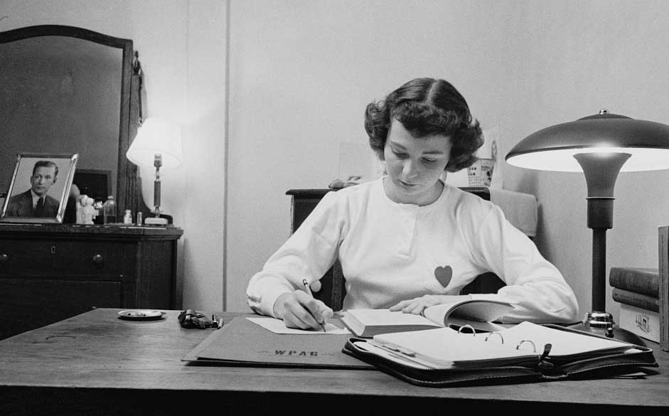 Black and white image of University of Michigan female student poring over books at her desk. A man's framed portrait is behind her on the dresser. (Image credit: Stanley Kubrick, Look magazine photograph collection, Library of Congress.)