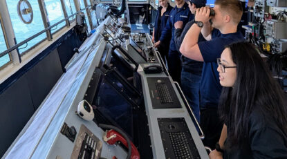 Members of the U-M Coast Guard Auxiliary view water through binoculars on a boat.