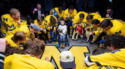 Members of the Michigan hockey team, dressed in maize jersyes, huddle around Block M in prayer with a young special-needs supporter named Conner.