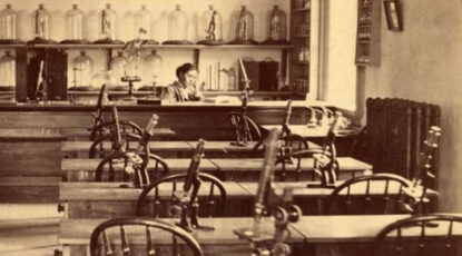 Sepia-toned image of woman scientist at University of Michigan surrounded by microscopes.