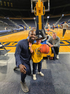 Michigan basketball coaches pose with young fan on the court at Crisler Arena.