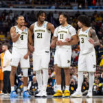 Four University of Michigan basketball players chat at center court.