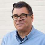 Headshot of caucasian man with dark hair and glasses wearing a blue oxford shirt. His name is Tom Kertscher.