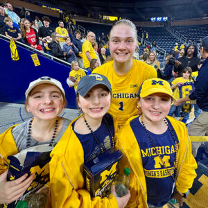 Michigan women's basketball player poses with triplets dressed head to toe in maize and blue.
