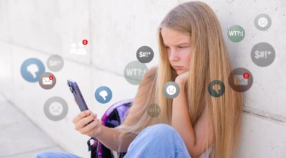 Teen girl looks at cellphone with furrowed brow while emojis swirl around her.