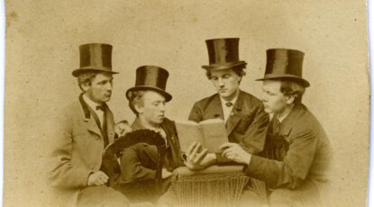 Four men in top hats peer at a book in a posed photograph, circa 1869.