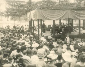 Sepia-toned image of crowd around a covered pavilion to view speaker and commencement exercises in 1912 at the University of Michigan, Ann Arbor.