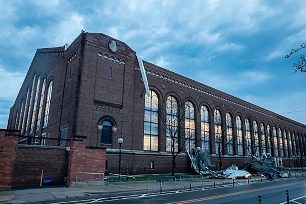 Image shows damage to Yost Ice Arena after two tornadoes touched down in Ann Arbor April 14, 2026. The first touched down at 1:44 a.m. near the Interstate 94 eastbound entrance ramp at Jackson Avenue. The second touched down two minutes later at the intersection of West William Street and Fourth Street near the Argus Building. The tornadoes were both EF1, which corresponds with winds of 86-110 mph. Pieces of the metal roof litter the sidewalk along State Streeet. (Image credit: Michigan Commons.)