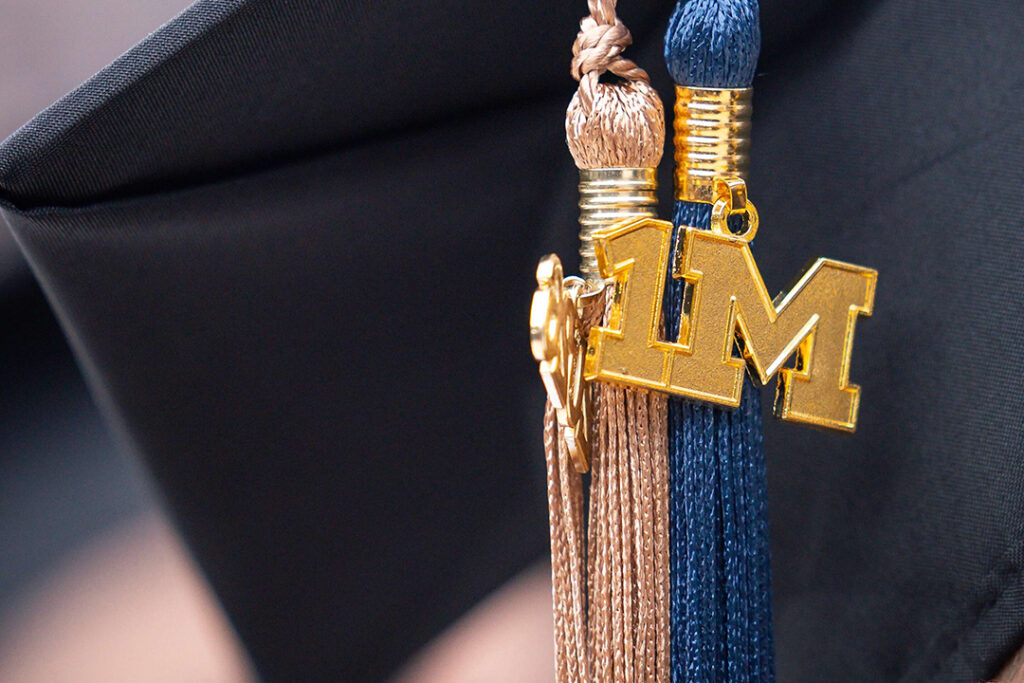 A medallion hanging from a commencement mortarboard features the number one and a block M to signify conferral of the 1 millionth degree from the University of Michigan.