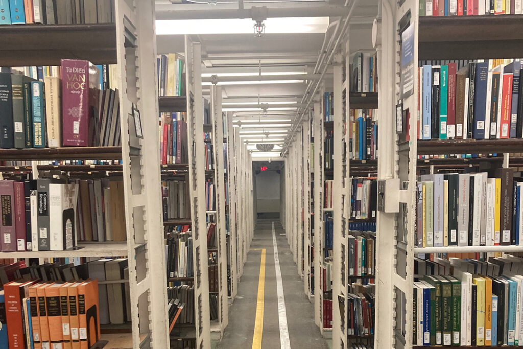 Interior of University of Michigan graduate library stacks. Long hallway with book-lined shelves on each side,