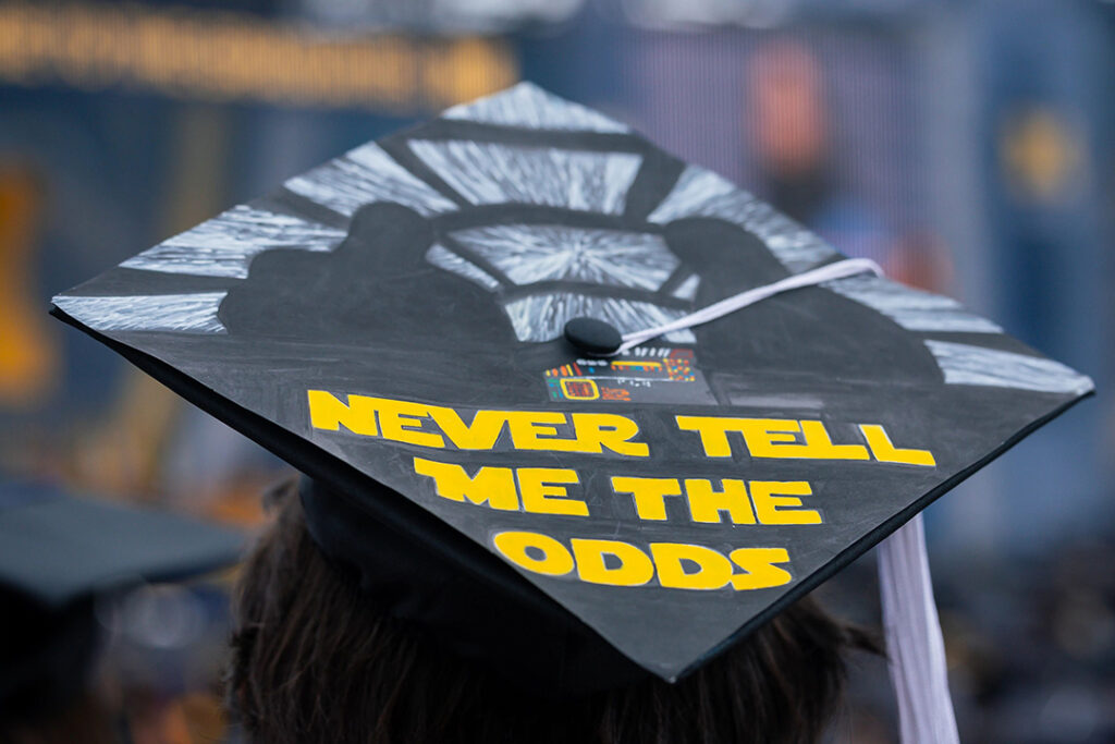 Top of a student's graduation mortarboard reads: Never tell me the odds. University of Michigan, Ann Arbor, 2026.