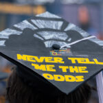 Top of a student's graduation mortarboard reads: Never tell me the odds. University of Michigan, Ann Arbor, 2026.