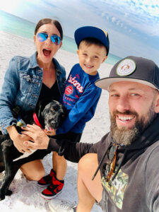 Caucasian family of mom, dad, and son on the beach with their dog.
