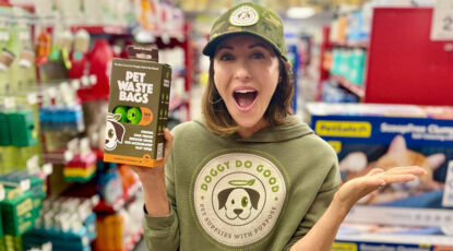 Cara AnnMarie, a caucasian actress and founder of Doggy Do Good stands in pet store dressed in branded gear holding a package of pet waste bags. She is a graduate of U-M in Ann Arbor.