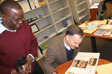 Joseph Ansong (standing) and Brian Arbic page through a scrapbook of Arbic's time as a Peace Corps volunteer in Ghana. Ansong was Arbic's student, and eventually made his way to U-M as a post-doctoral student, where his office is next door to Professor Arbic's. (Photo: William Foreman.)