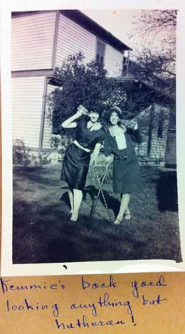 A black and white photo of two young women laughing and drinking from beer bottles in a back yard.