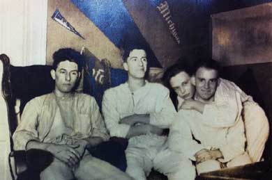 A black and white photo of four young men slouching together on a couch.