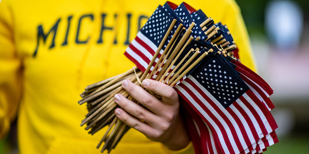 A student in a maize Michigan sweatshirt holds a handful of small flags.