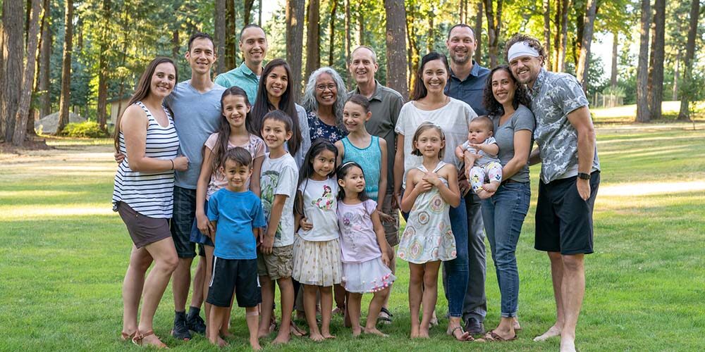 Portrait of a senior couple posing for a photograph with their adult children and grandchildren. The multi-ethnic and multi-generation group is gathered at a family reunion. The family members affectionately have their arms around one another and are smiling. They are standing in a grassy meadow with trees in the background. Stock photo