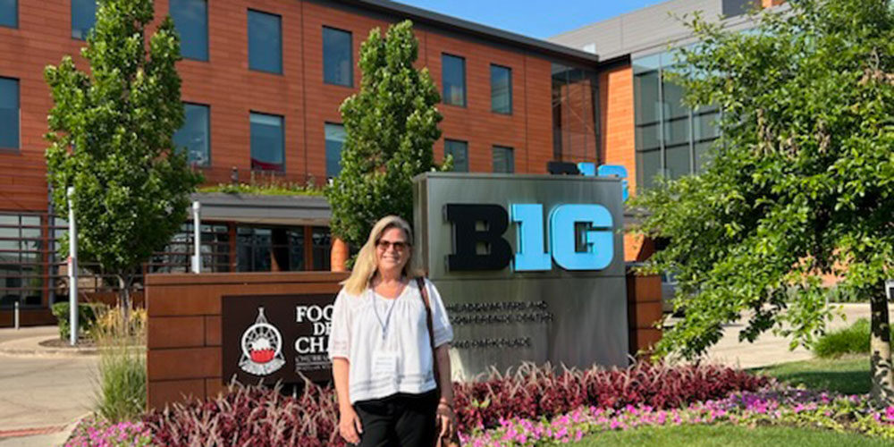 Woman stands at Big 10 headquarters sign.