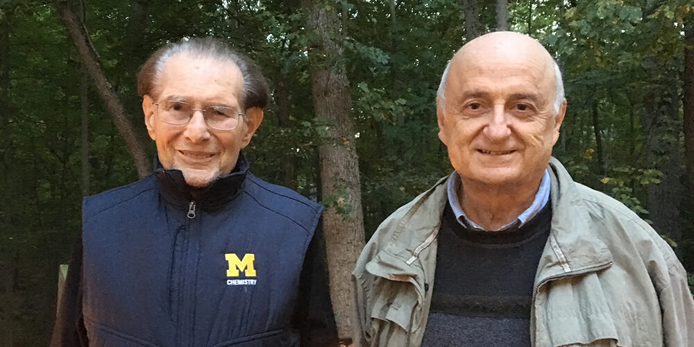 Two caucasian men, Raoul Kopelman and his mentee Panos Agryakis, stand side by side with trees behind them.