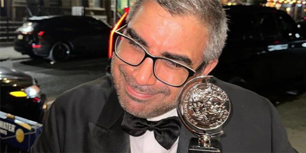 Tony winner Mike Mosallam, wearing glasses and with salt-and-pepper hair, cradles Tony award.