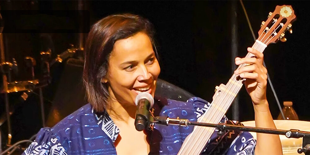 Beautiful woman, artist in residence at University of Michigan, plays bass guitar while seated at a microphone