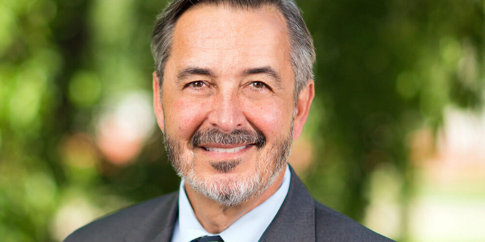 Headshot of caucasian-looking man, UM-Dearborn's Dominic Grasso, with salt-and-pepper hair, a beard, and a pleaseant smile. He is new interim president of U-M.