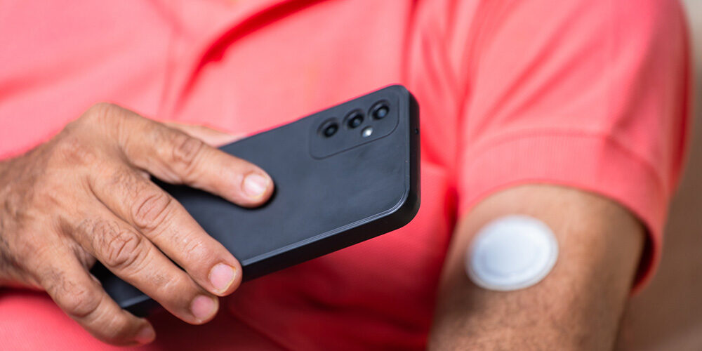 Person checks blood glucose levels using device on the body and a cellphone.
