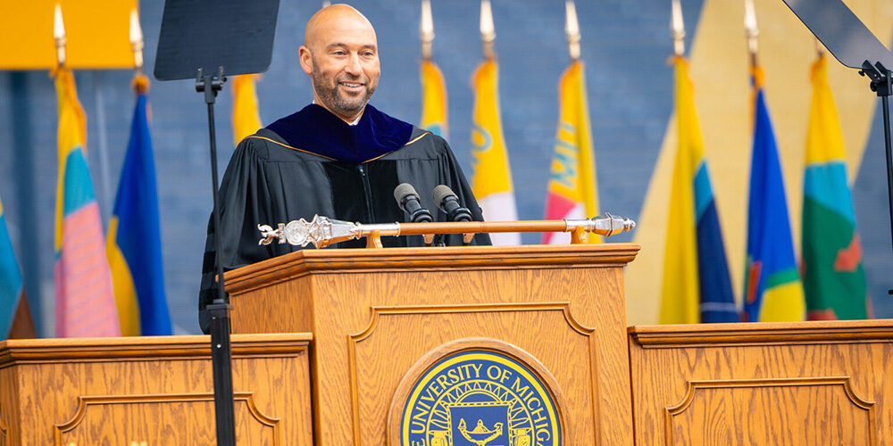 Derek Jeter speaks from the dais at Michigan Commencement dressed in all the graduation regailia.