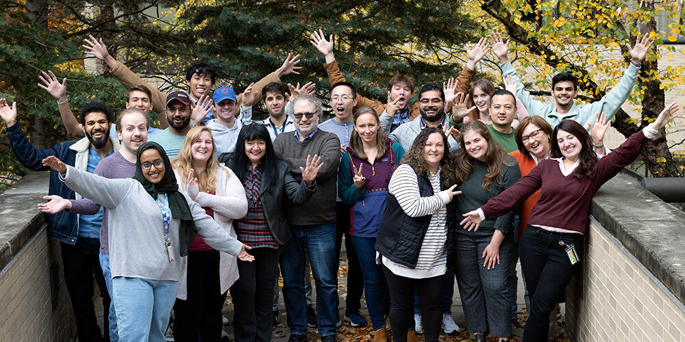 A team of happy researchers poses together outside on a sunny day.
