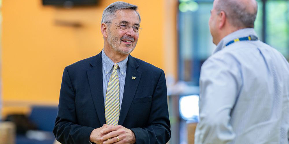 U-M President Domenico Grasso speaks to a man who is seen from behind.