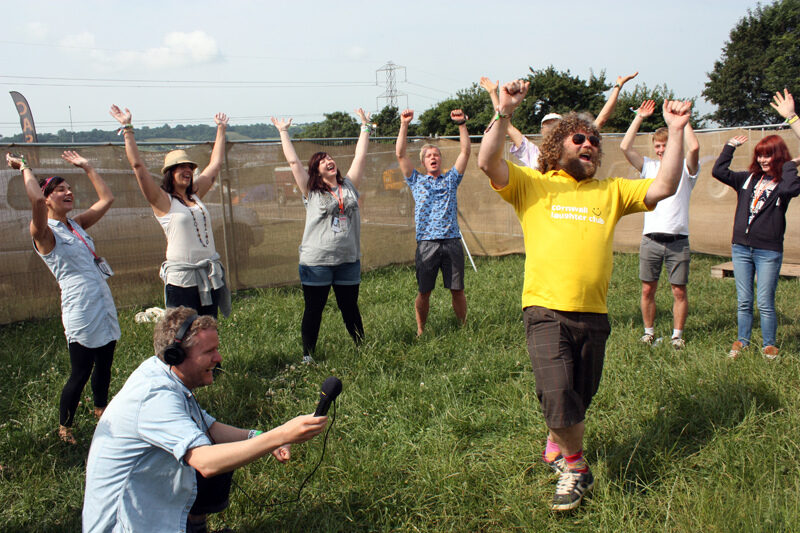 Group of people do laughing yoga in an outdoor venue.