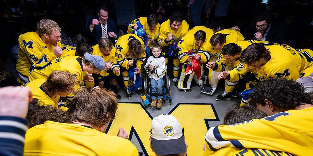 Members of the Michigan hockey team, dressed in maize jersyes, huddle around Block M in prayer with a young special-needs supporter named Conner.