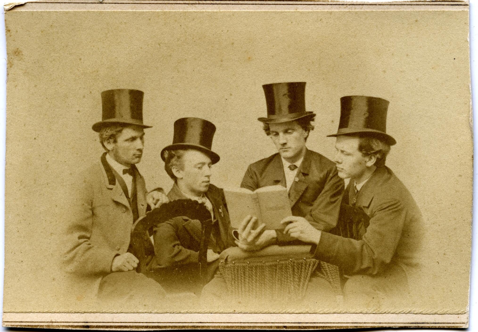 Four men in top hats peer at a book in a posed photograph, circa 1869.